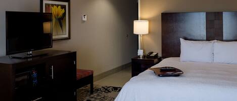 Habitación de hotel con cama, televisor, escritorio con lámpara y detector de incendios en la pared.