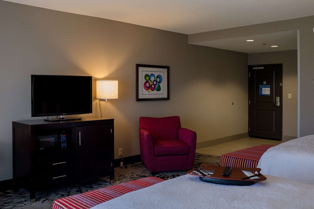 A hotel room with a flat-screen TV, a red armchair, a bed with a white comforter, and a small table with a tray.