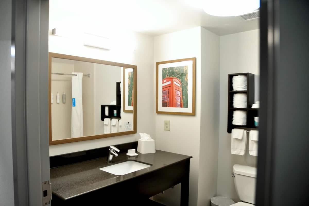 A modern bathroom with a large mirror, a sink, a toilet, and a shelf with towels.
