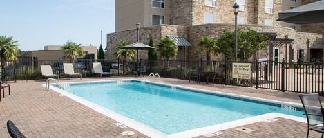 A rectangular swimming pool with a brick deck, surrounded by lounge chairs and a fence.