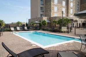 A rectangular swimming pool with a brick deck, surrounded by lounge chairs and a fence.