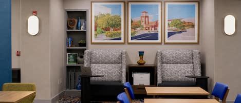 Uma sala de conferências com duas cadeiras, uma mesa, uma estante e três quadros na parede.