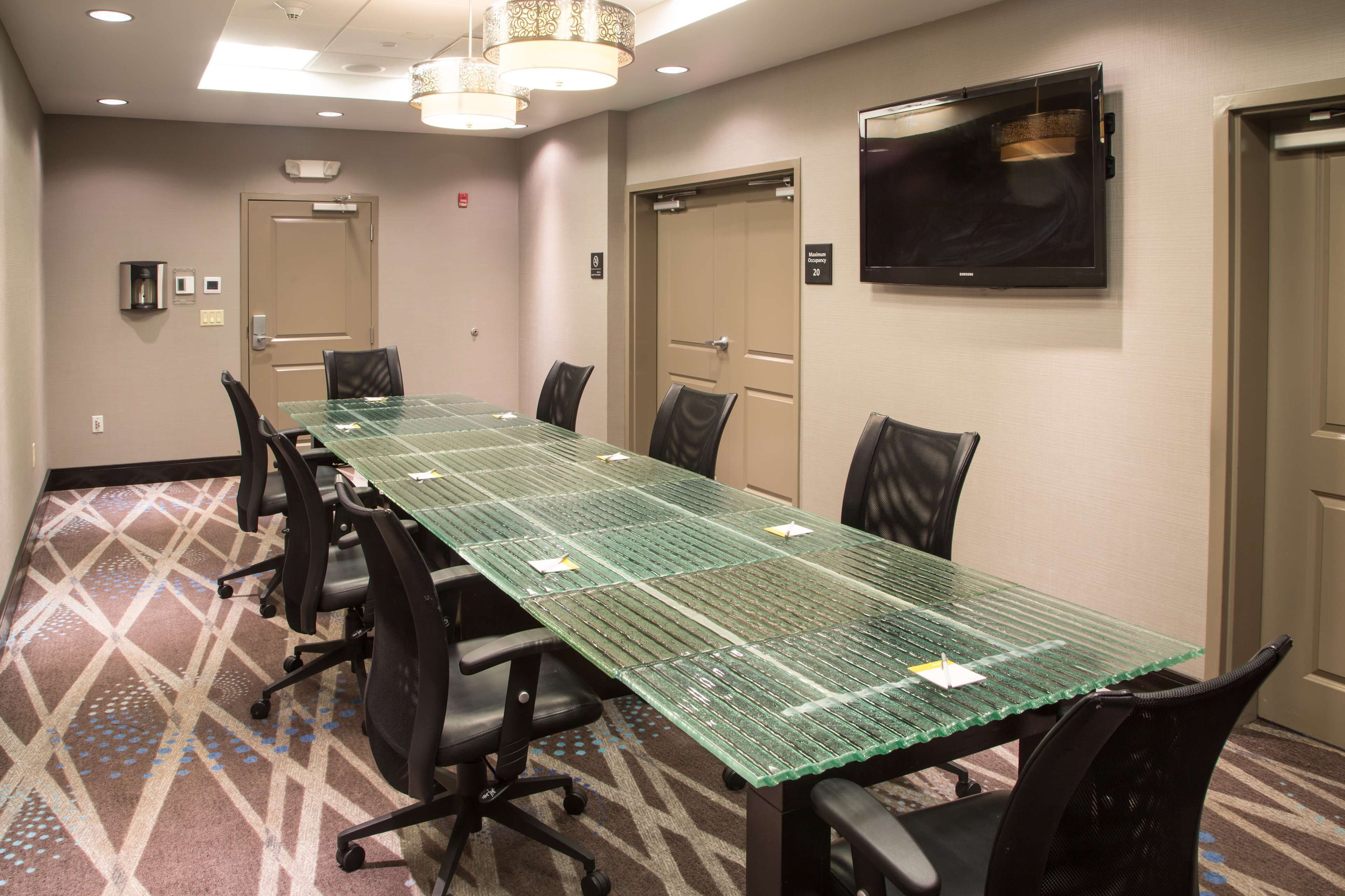 A conference room with a long table, black chairs, a flat-screen TV, and a patterned carpet.
