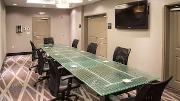 A conference room with a long table, black chairs, a flat-screen TV, and a patterned carpet.