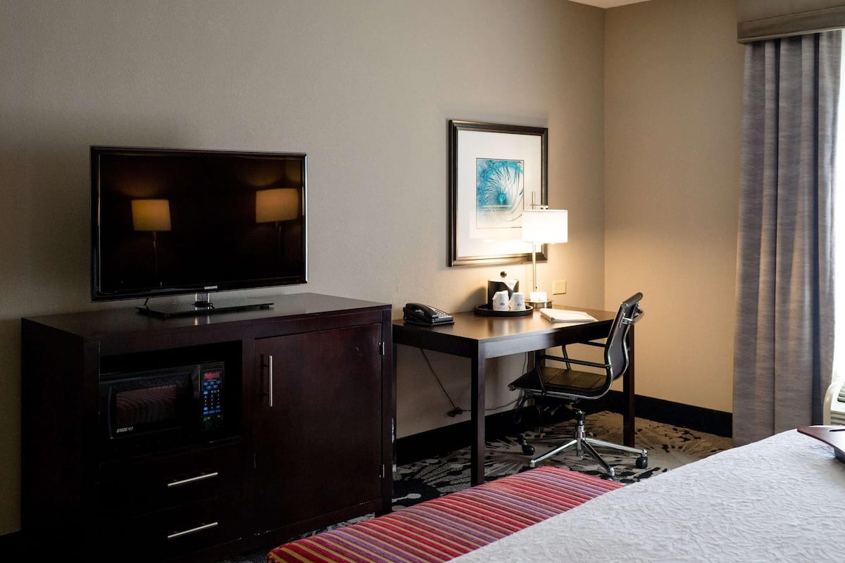 A hotel room with a bed, a desk with a lamp, a television, a microwave, and a telephone.