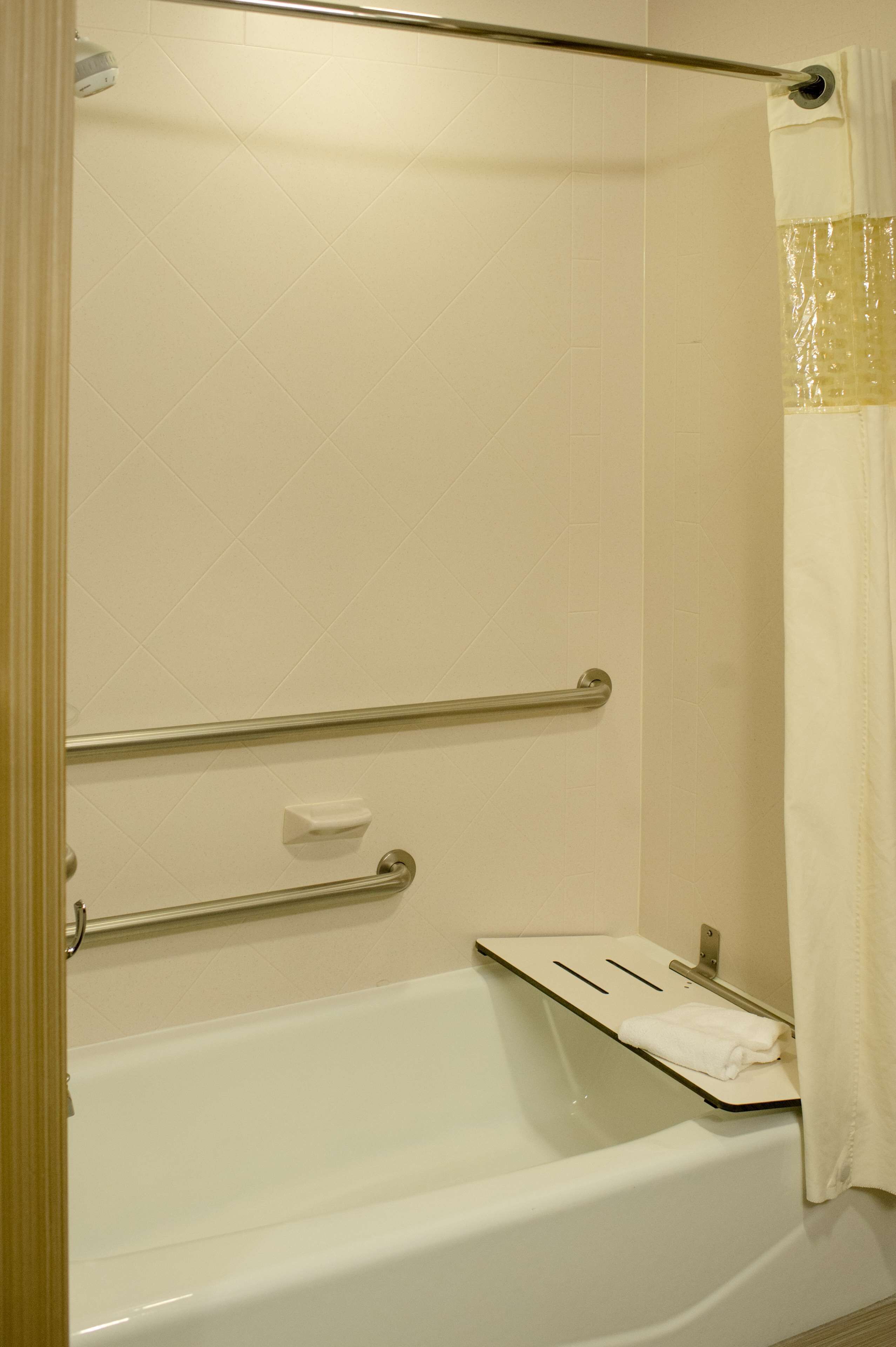 A bathroom with a white bathtub, grab bars, a towel rack, and a shower curtain.