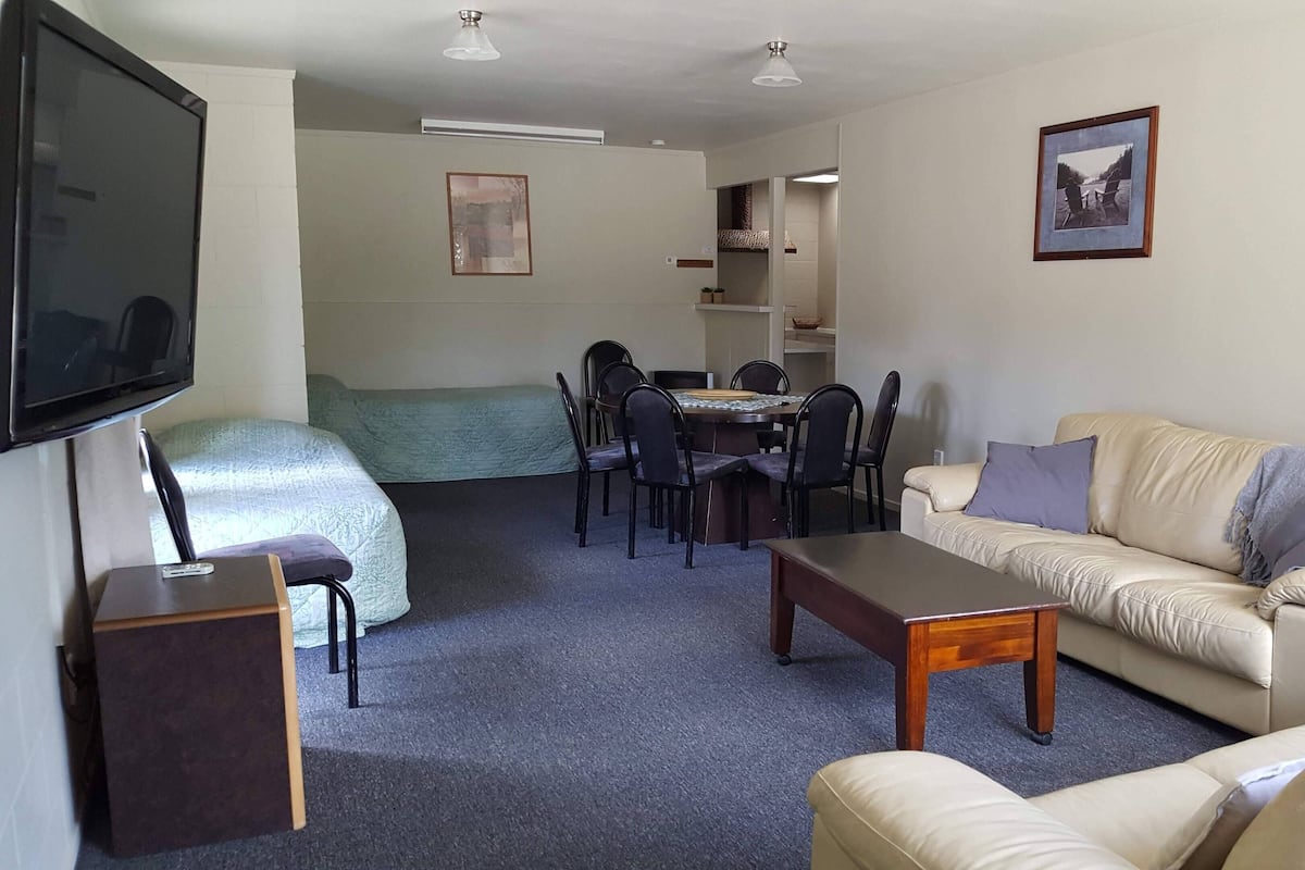 A living room with a TV, sofa, coffee table, and a dining area with chairs and a table.