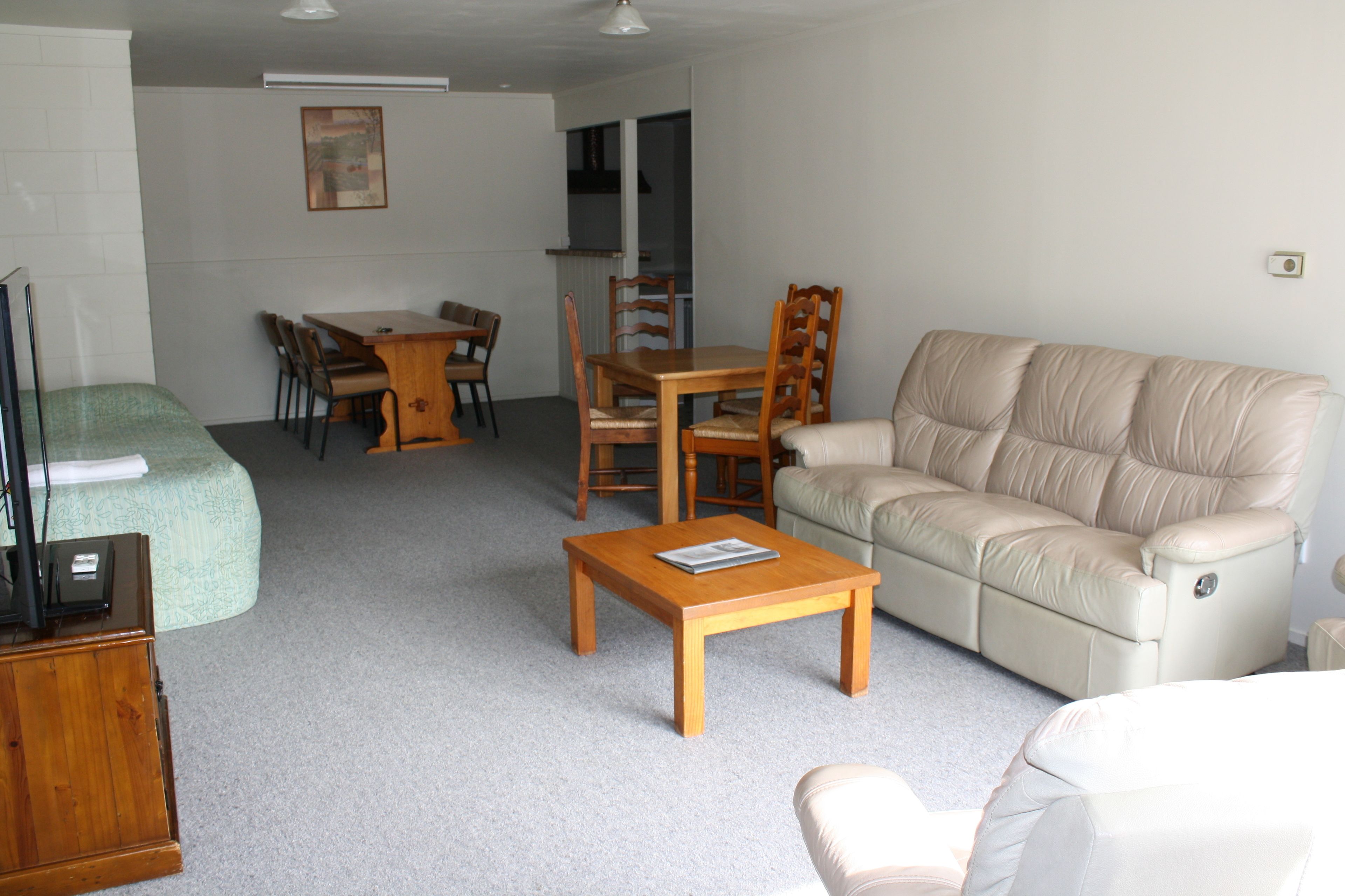 A living room with a beige sofa, wooden coffee table, and a dining area with a wooden table and chairs.