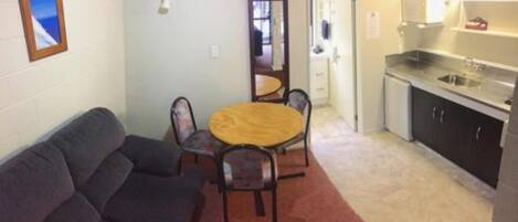A compact living space with a sofa, a round dining table, and a kitchenette.