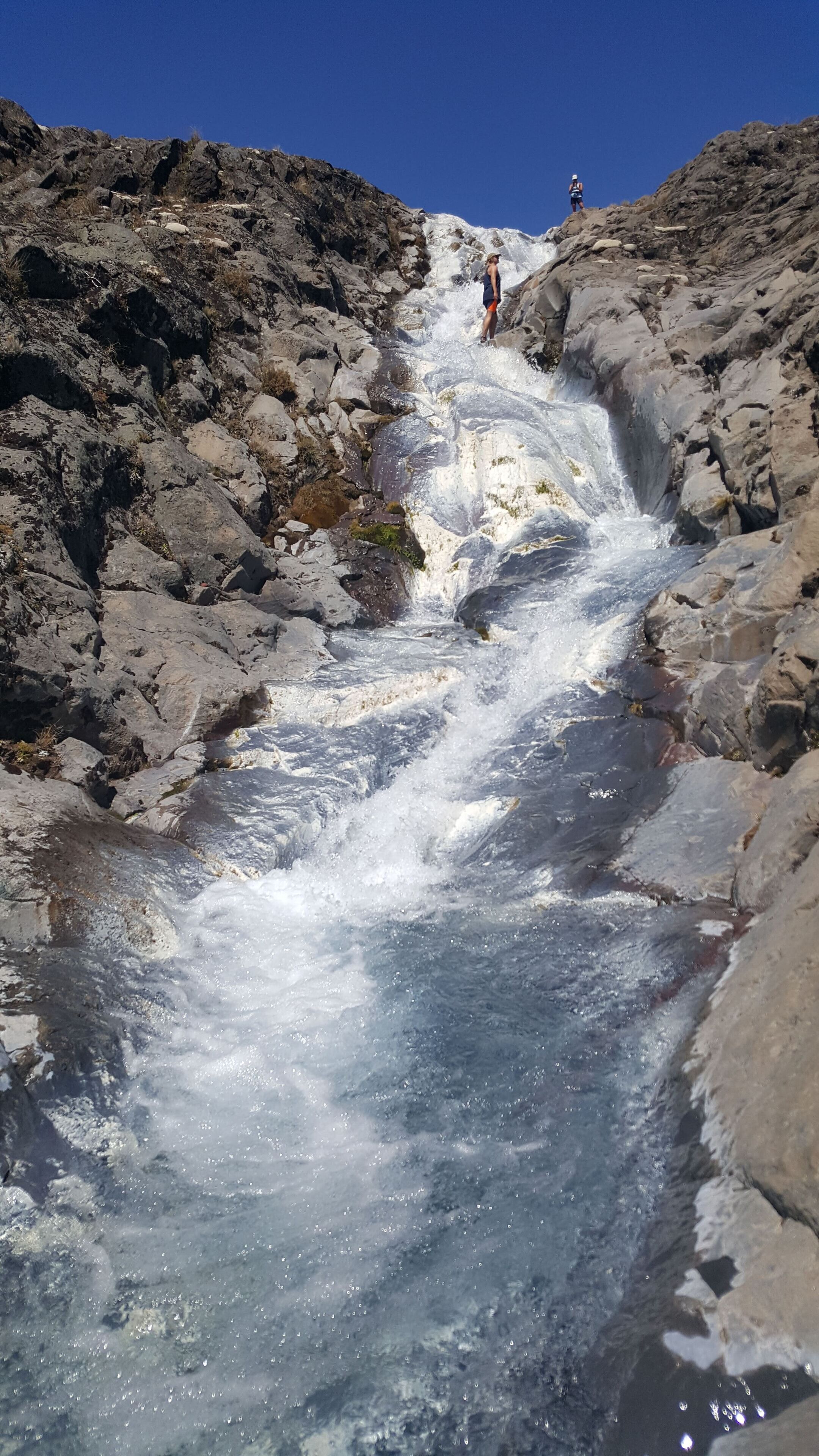 A rocky waterfall with two people standing at the top.