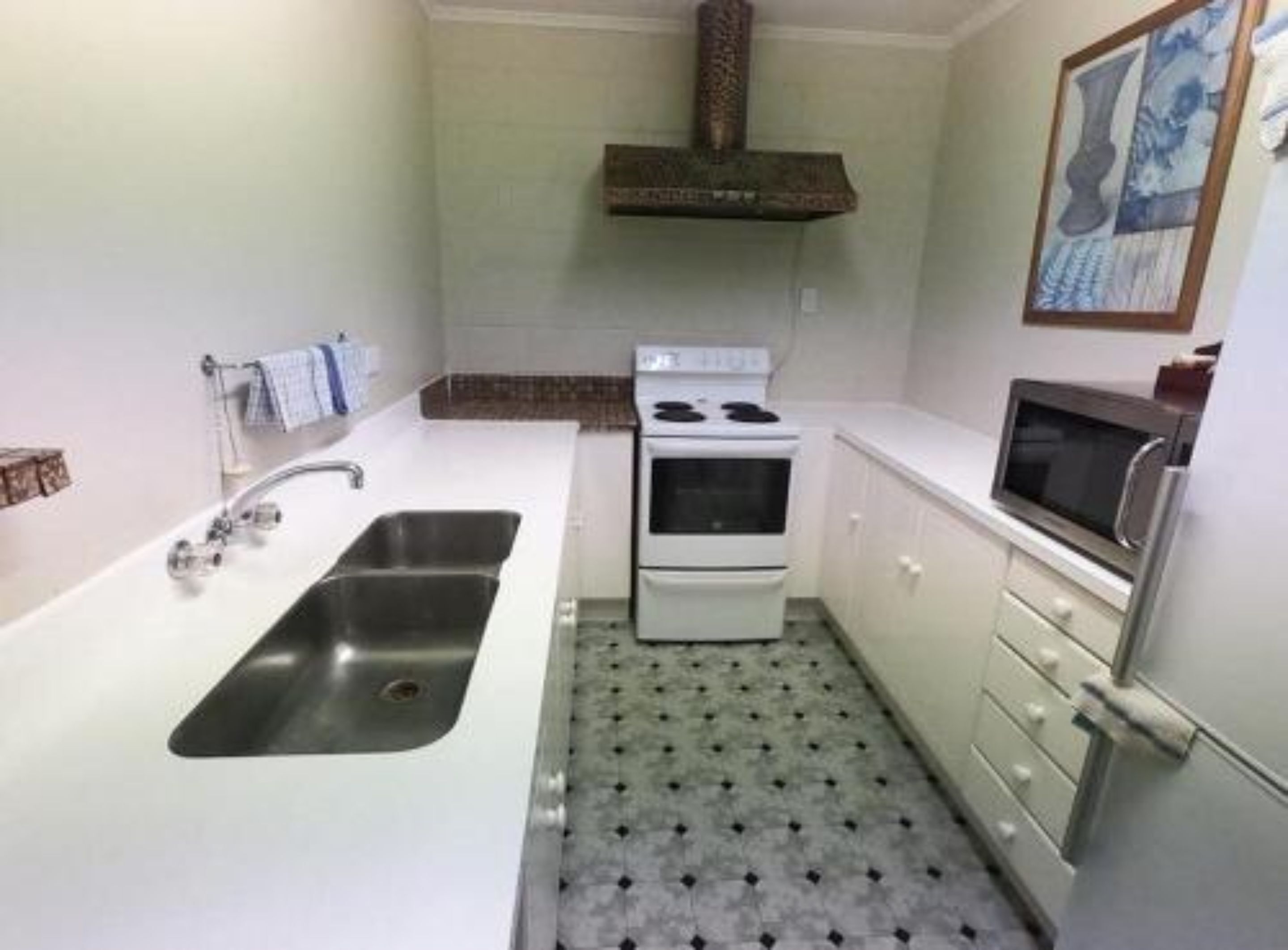 Cocina compacta con pileta, estufa, microondas y piso estampado.