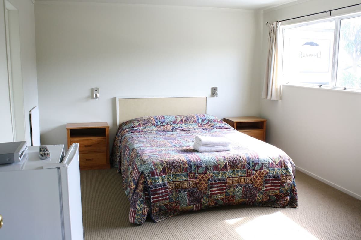 A bedroom with a bed, two bedside tables, a desk, and a window with curtains.