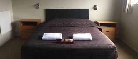 A neatly made bed with two towels, a small tray with a bottle and a glass, and two wooden nightstands.
