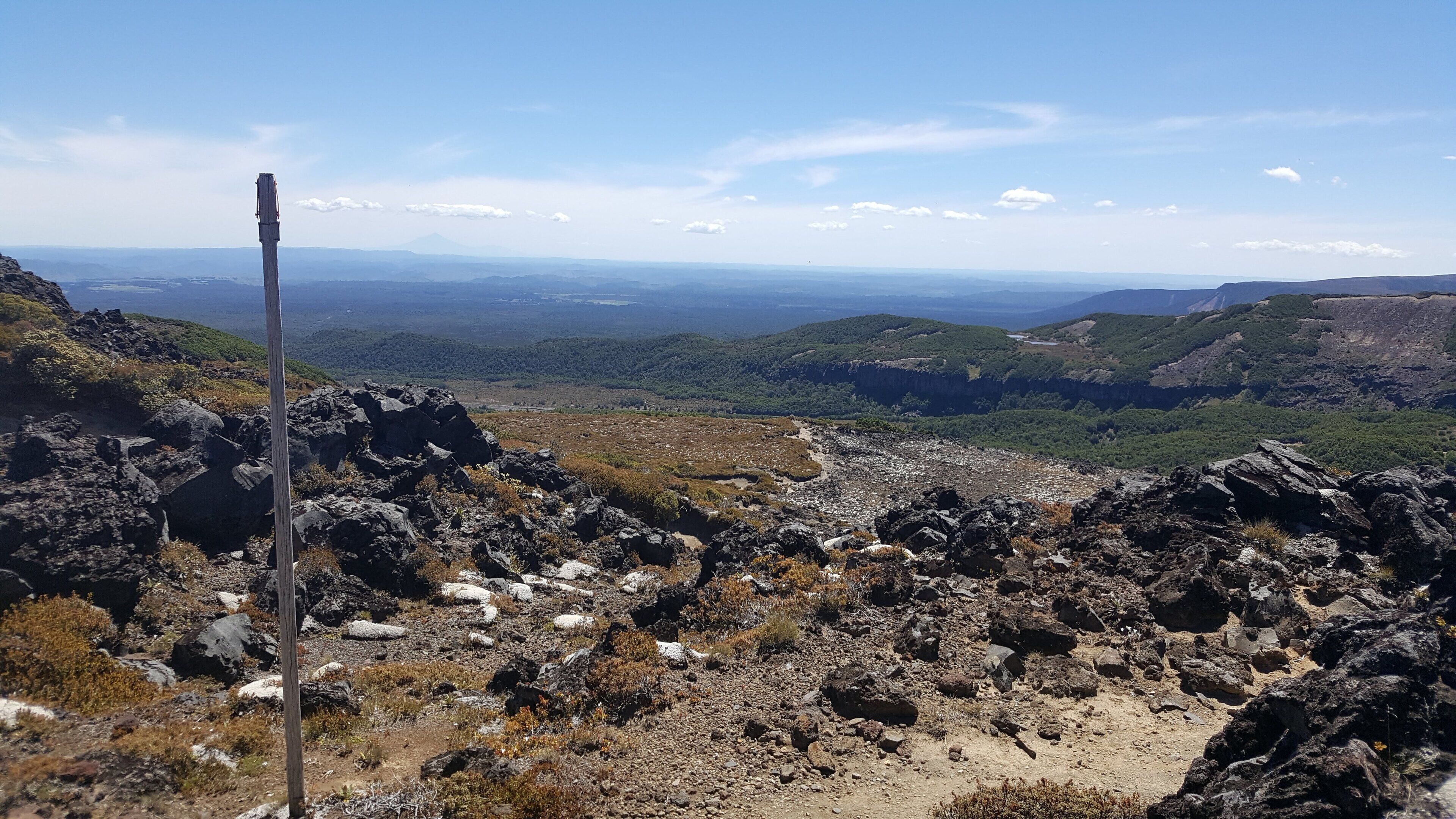 A rocky landscape with a wooden post, a clear sky, and distant hills.