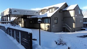 Ein Gebäude mit der Aufschrift „Ruapehu Mountain Motel & Lodge“, mit einem überdachten Eingang, einer Treppe und einem mit Schnee bedeckten Gelände.