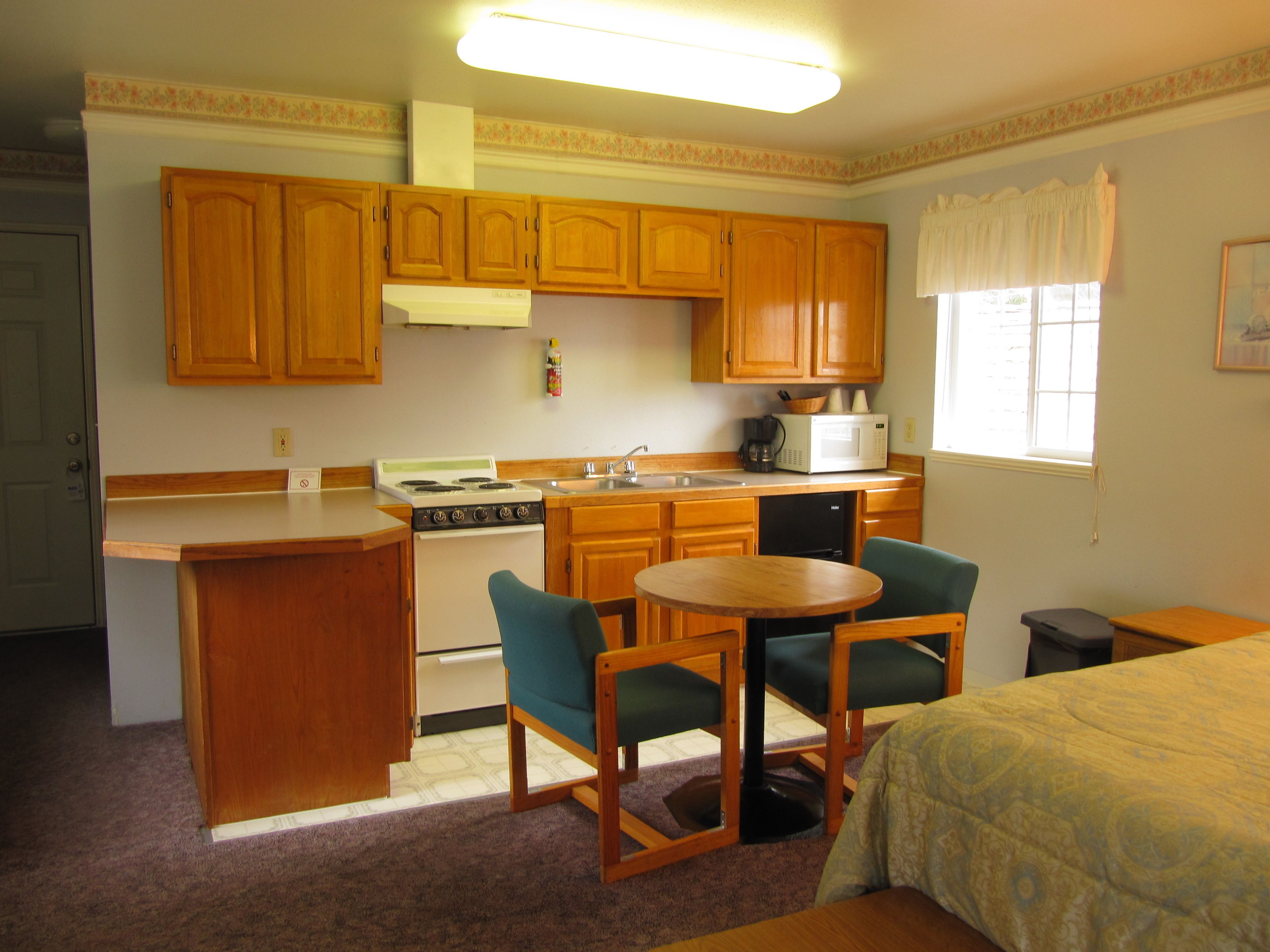 A compact kitchen with wooden cabinets, a stove, a microwave, and a sink. There is a small dining area with a table and chairs.