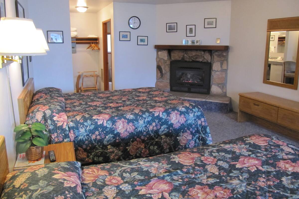 Un dormitorio con dos camas, una chimenea, un espejo y un reloj en la pared.