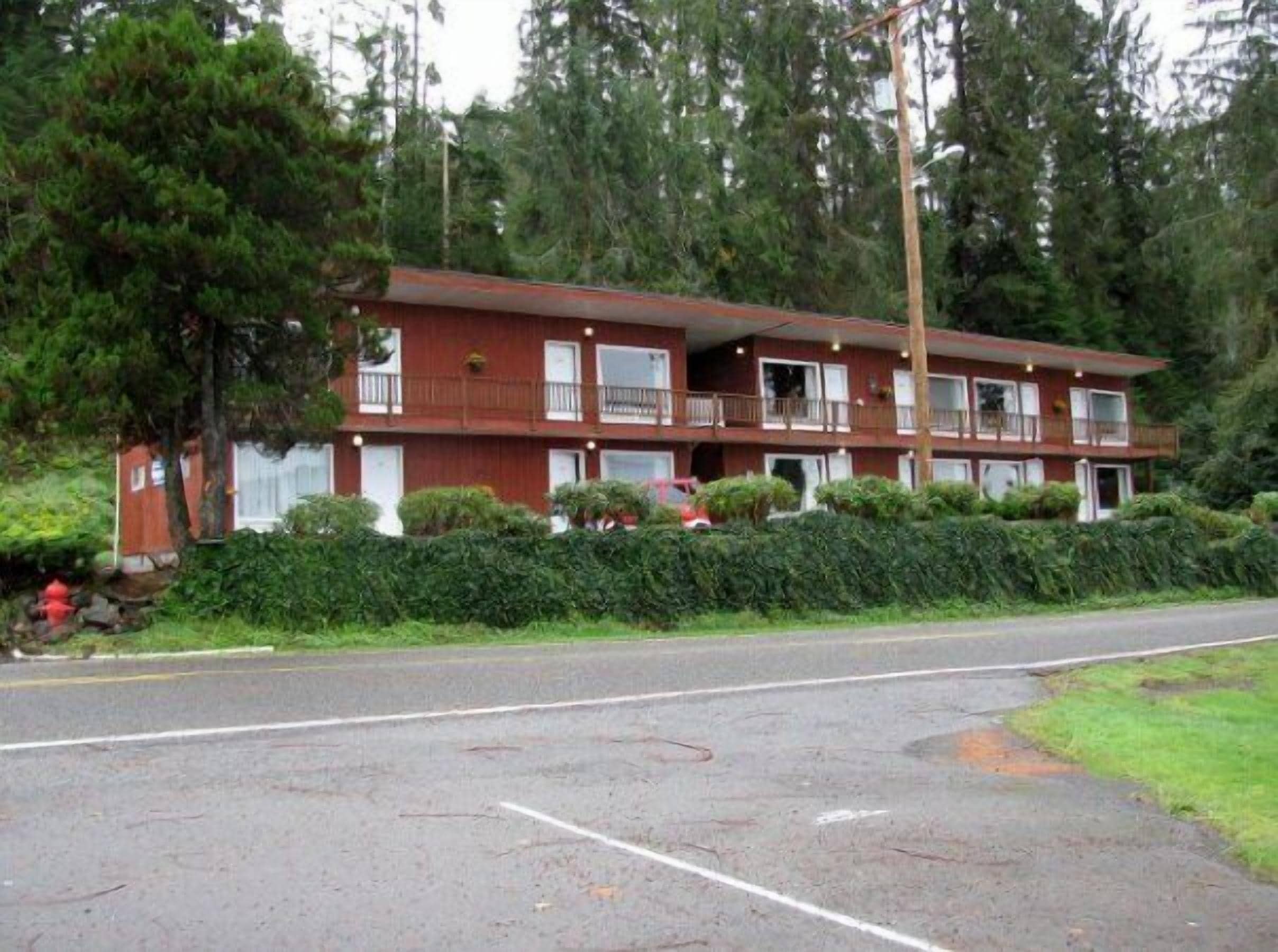 A multi-story motel with a red exterior, multiple balconies, and a parking lot in front.