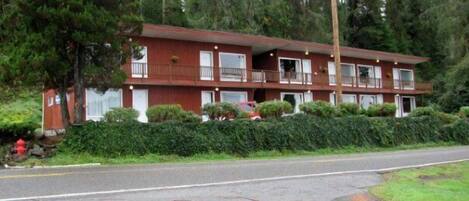 A multi-story motel with a red exterior, multiple balconies, and a parking lot in front.