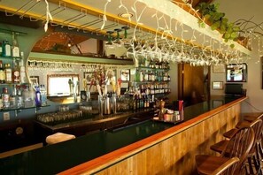 A bar area with a wooden counter, shelves with bottles, and hanging glassware. - Rain Forest Resort Village (Quinault)