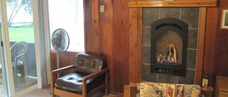 A cozy living room with a fireplace, a leather chair, and a fan.