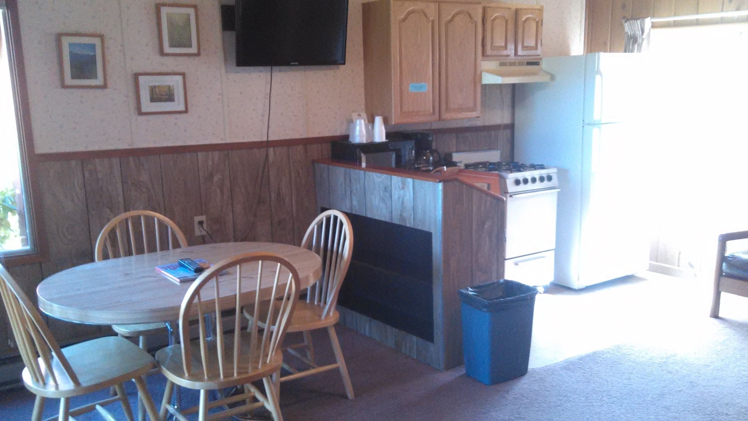 A compact kitchen with a dining area, wooden cabinets, a stove, and a TV mounted on the wall.