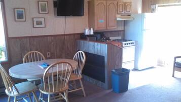 A compact kitchen with a dining area, wooden cabinets, a stove, and a TV mounted on the wall.