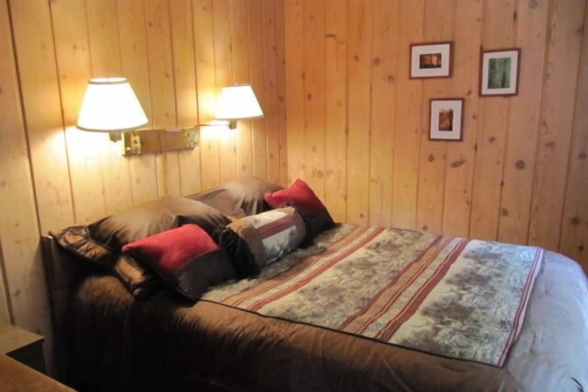 Una habitación con paneles de madera, una cama, dos lámparas fijadas a la pared y tres cuadros enmarcados.