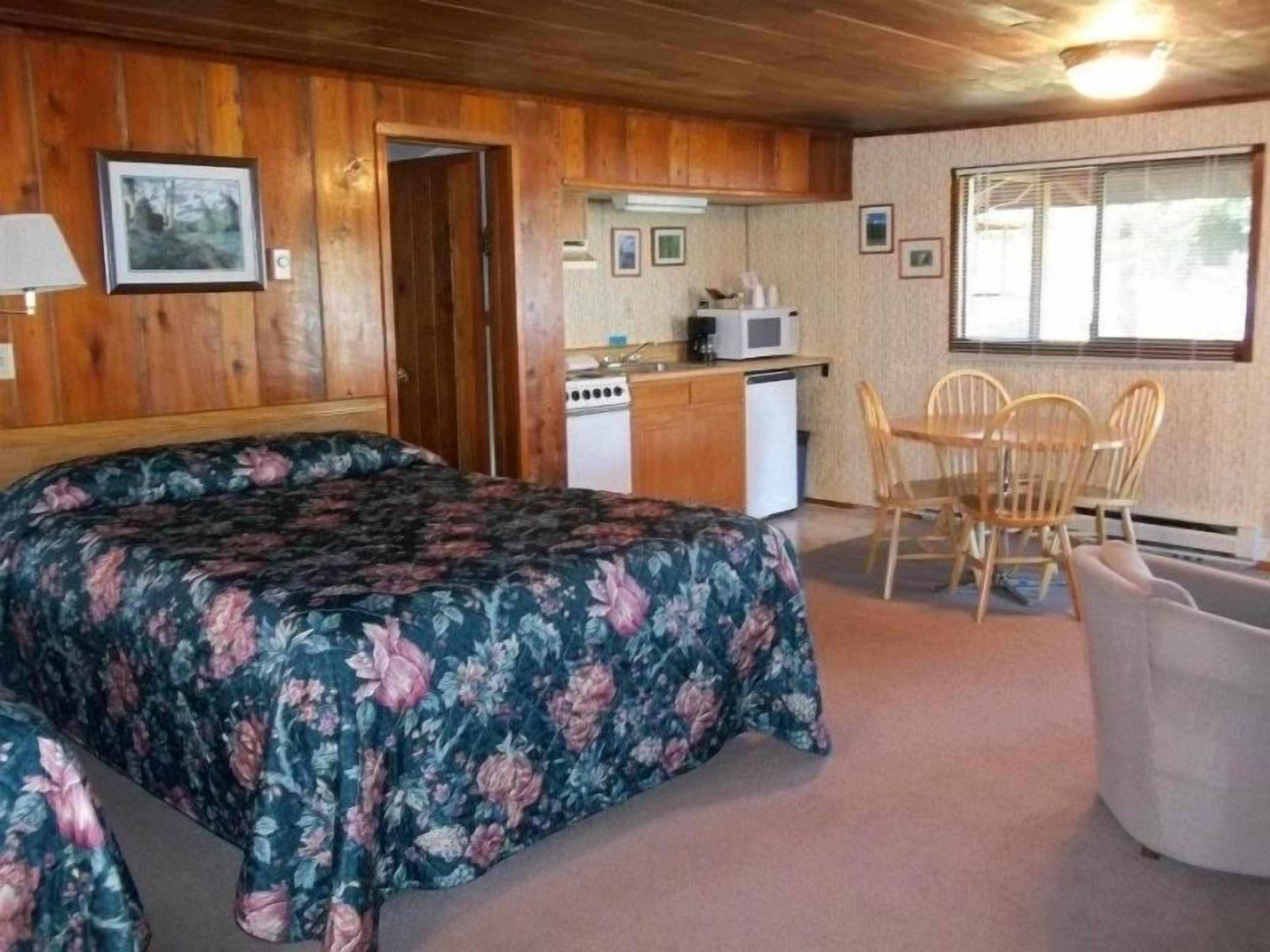A room with a bed, a small kitchenette, a dining table with chairs, and a window.