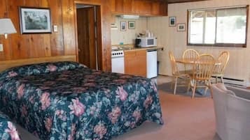 A room with a bed, a small kitchenette, a dining table with chairs, and a window.