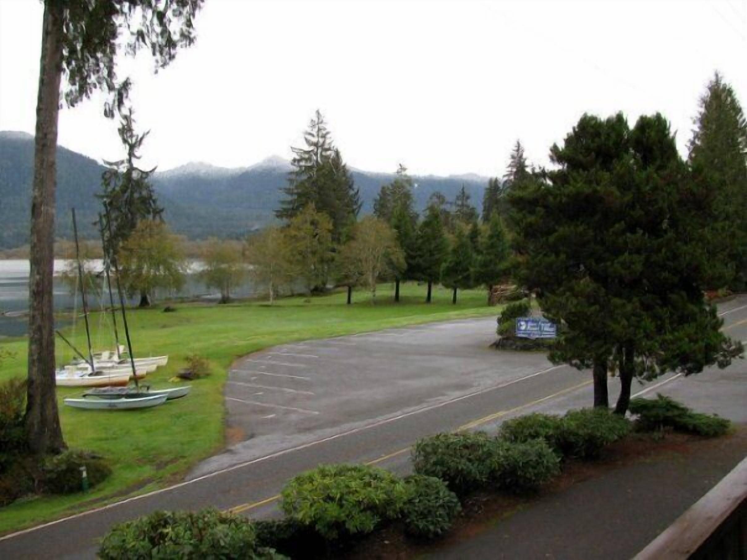 A road curving through a park with a lake and mountains in the background.