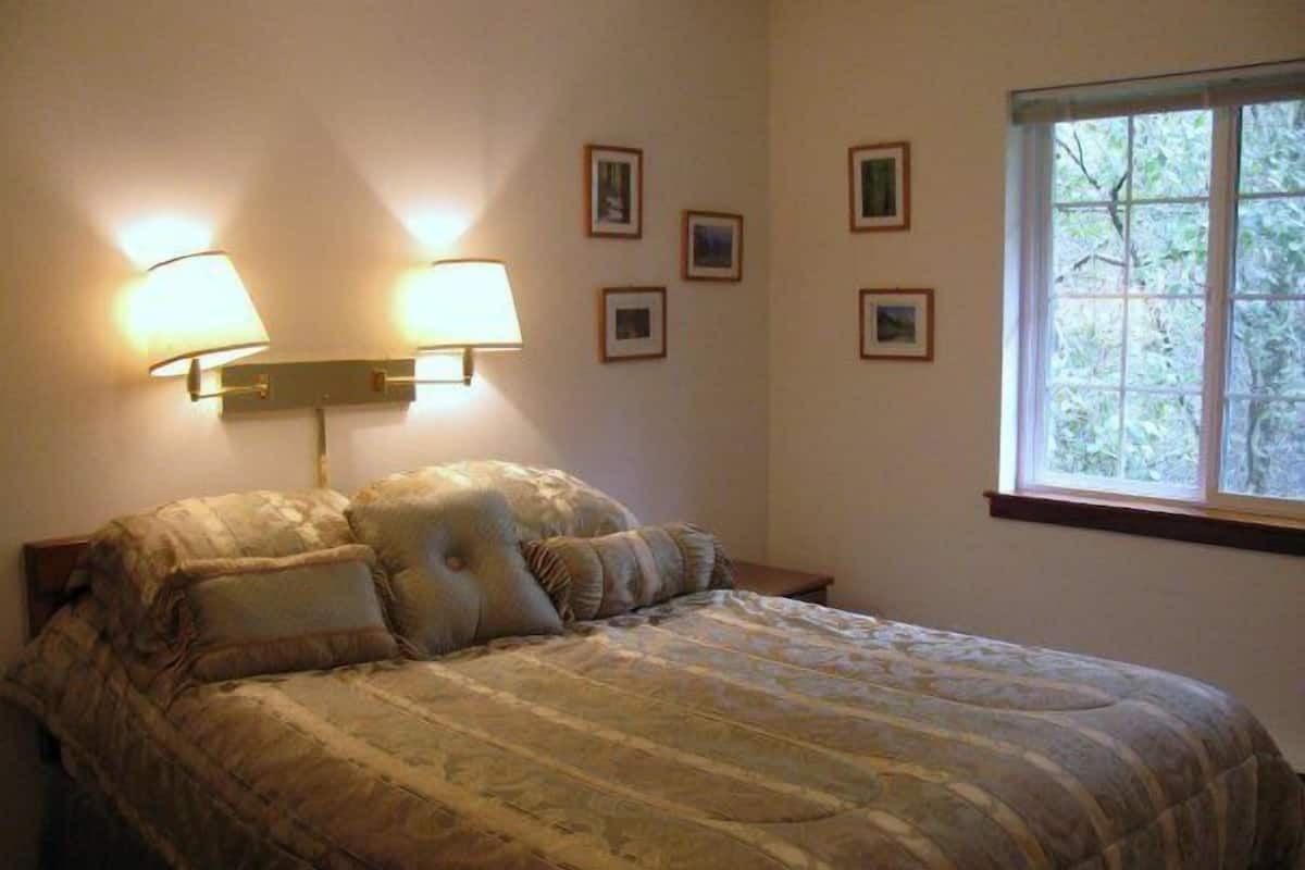 Un dormitorio con una cama grande, dos lámparas de pared y una ventana con vistas a árboles.