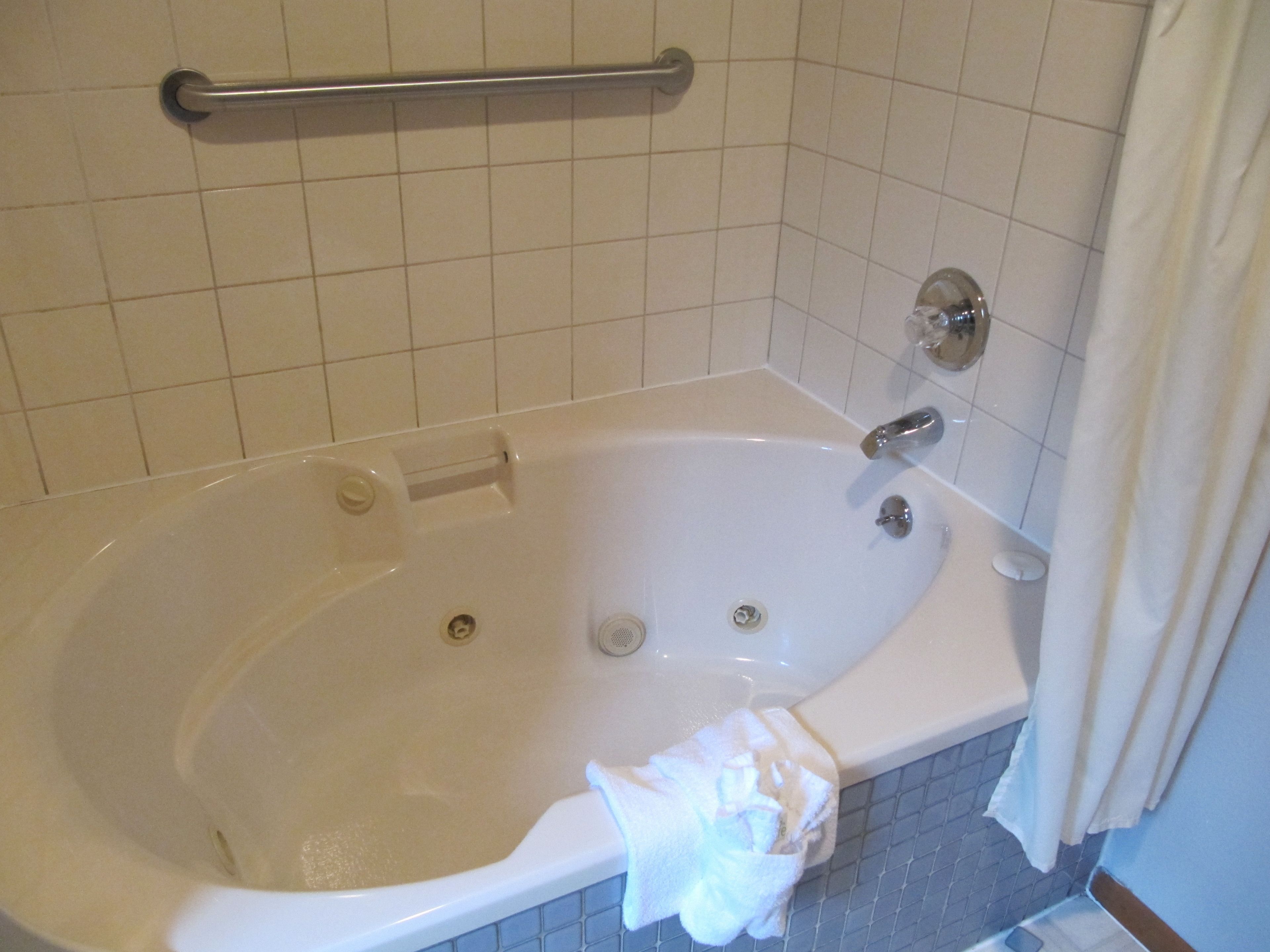 Una bañera estándar con una barra de apoyo, un cortinero y un revestimiento de azulejos.