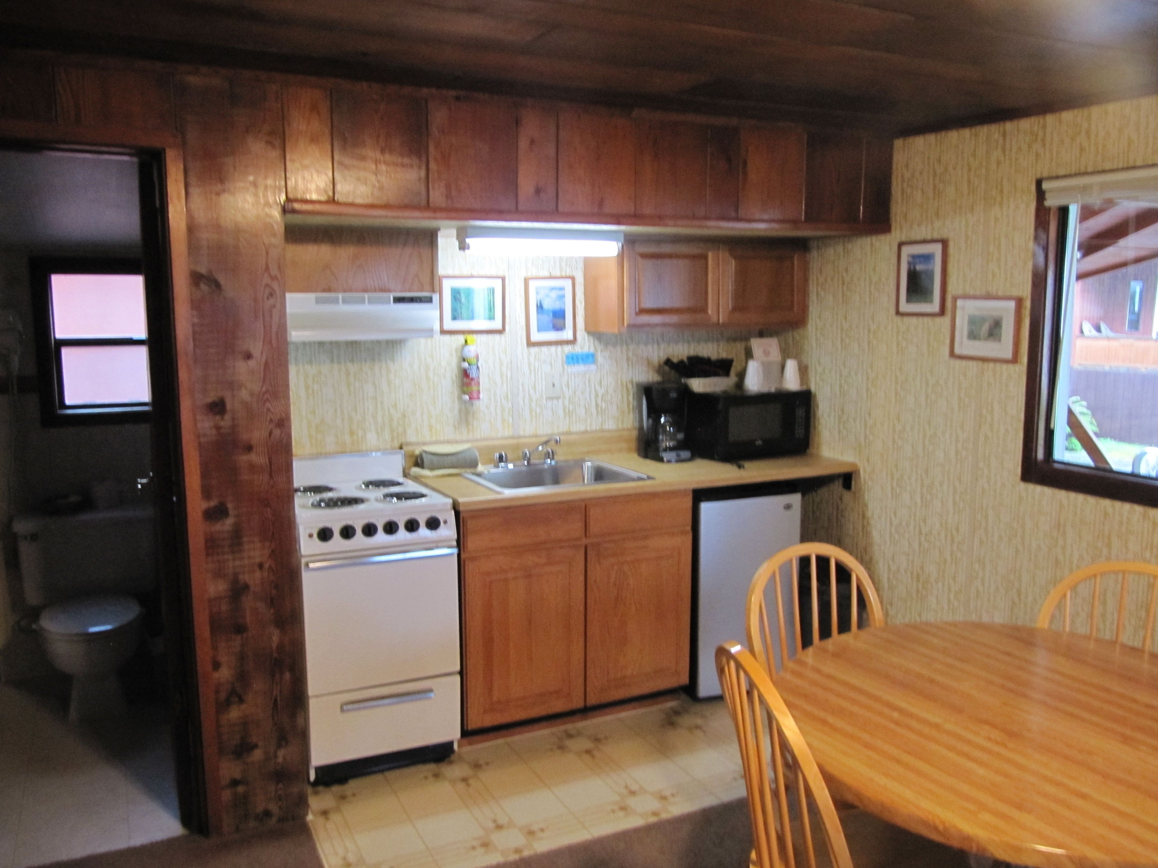 A compact kitchen with wooden cabinets, a stove, a microwave, and a sink.