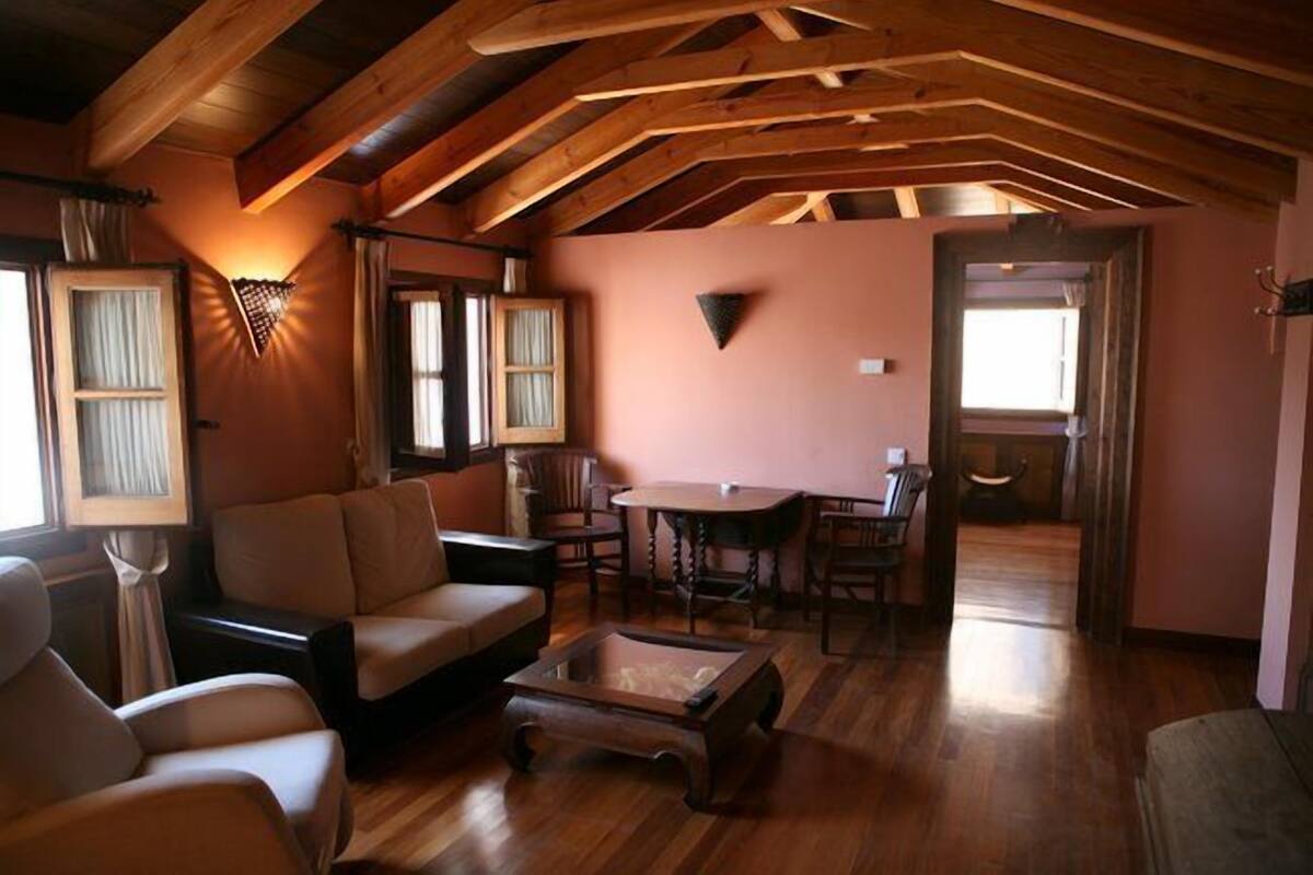 Ein gemütliches Wohnzimmer mit Holzbalkendecke, einer Couch, einem Couchtisch und einem Essbereich mit Stühlen und Tisch.