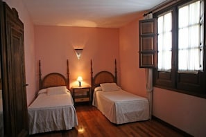 Une chambre avec deux lits simples, une table de chevet avec une lampe, une fenêtre avec des rideaux et une armoire en bois.