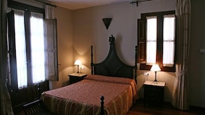 A bedroom with a wooden bed, two bedside tables with lamps, and a window with curtains. - La Colegiata de Ronda (Ronda)