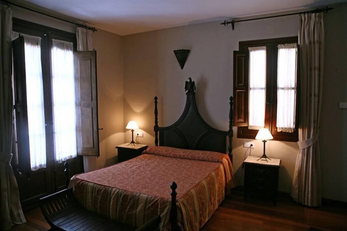 Ein Schlafzimmer mit einem hölzernen Bett, zwei Nachttischen mit Lampen und einem Fenster mit Vorhängen.