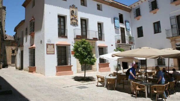 A courtyard with outdoor seating, a small tree, and a building with balconies and windows. - La Colegiata de Ronda (Ronda)