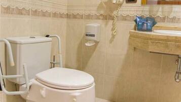 A bathroom with a toilet, a handrail, a soap dispenser, and a sink.