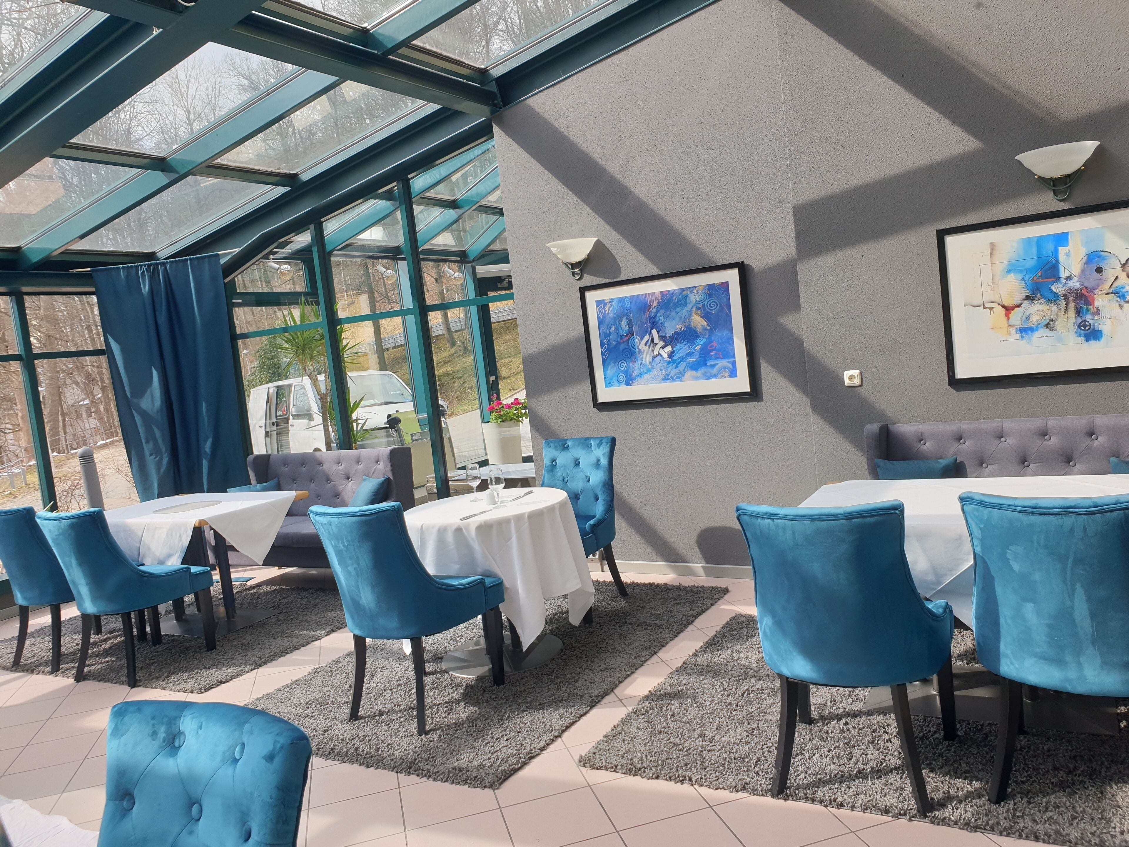 Un restaurante con sillas y mesas tapizadas en azul, un techo de cristal y un cuadro abstracto enmarcado en la pared.