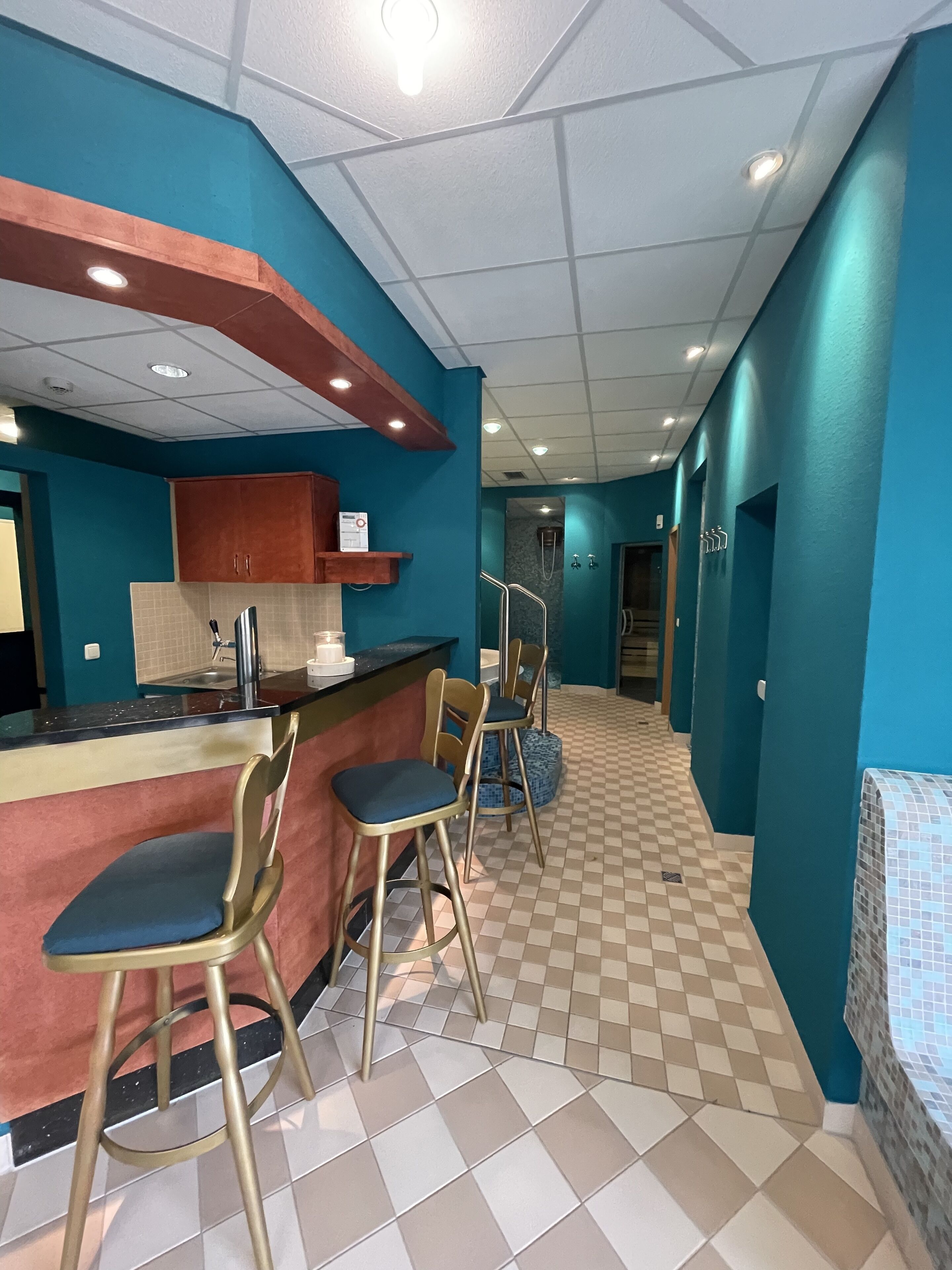A bar area with stools and a counter, a kitchen with cabinets and a sink, and a checkered floor.
