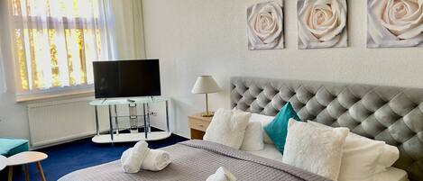 A hotel room with a bed, a TV, a desk, and artwork on the wall.