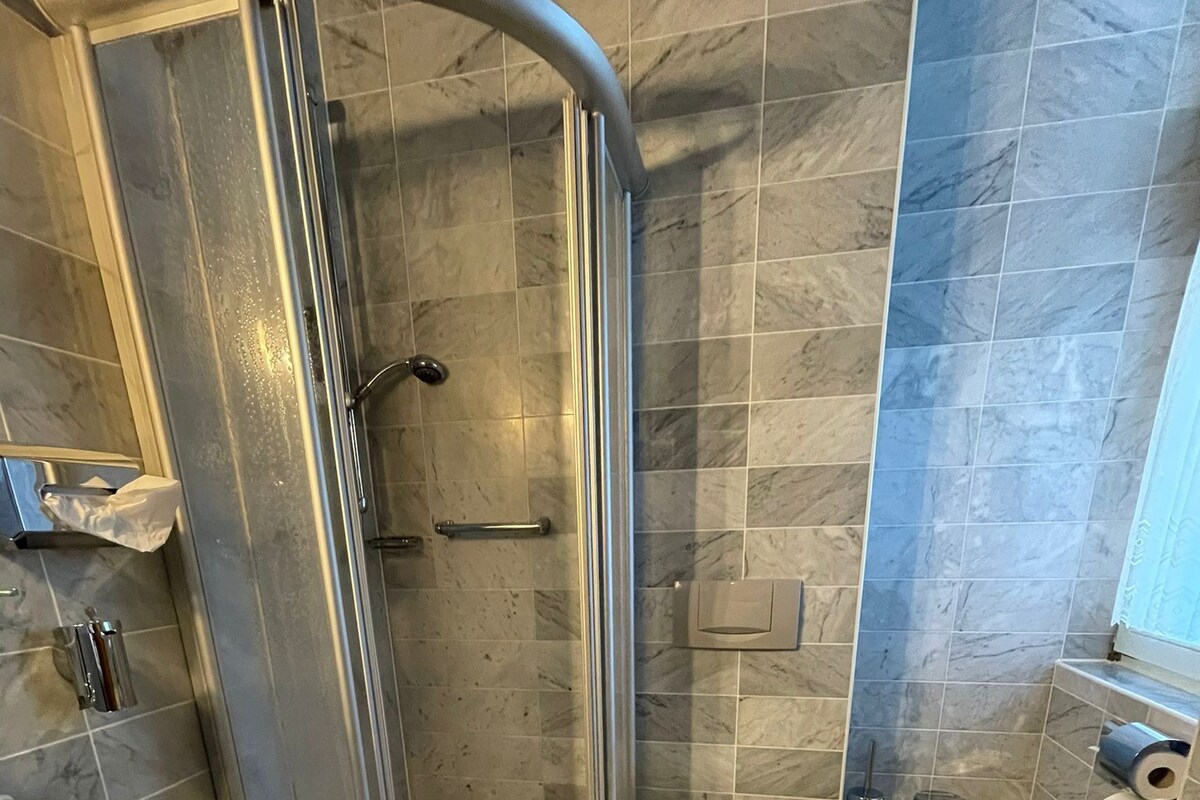 A bathroom with a shower, toilet, sink, and a small stool.