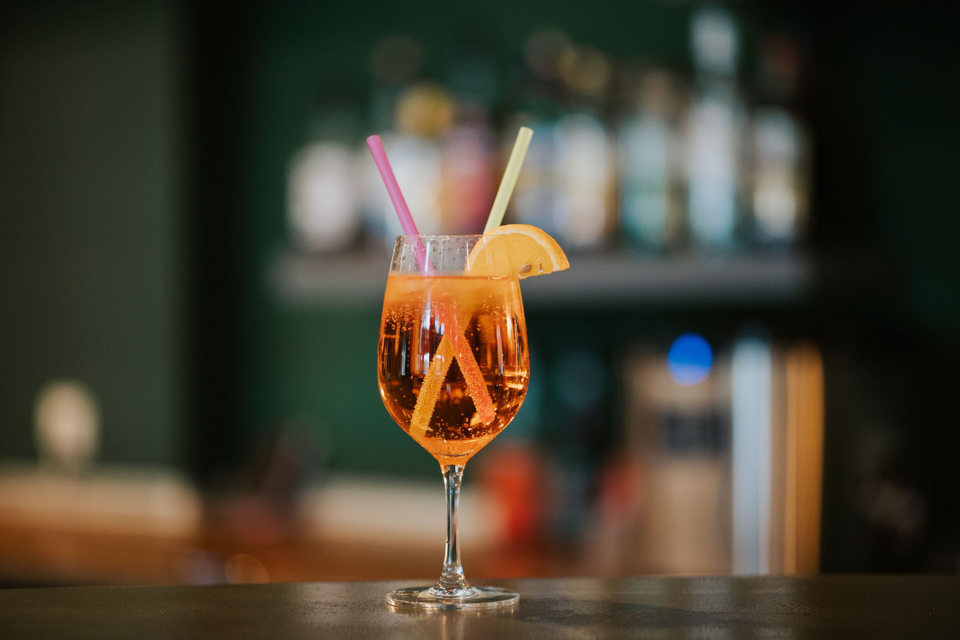Um cocktail com uma fatia de limão e canudos num copo sobre o balcão do bar.