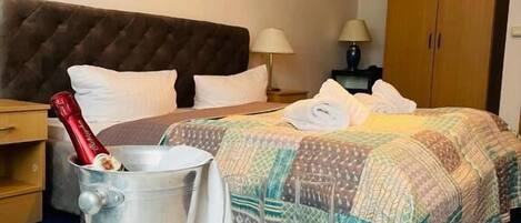 A hotel room with a bed, a bedside table with a champagne bottle and glasses, a nightstand, a lamp, and a wardrobe.