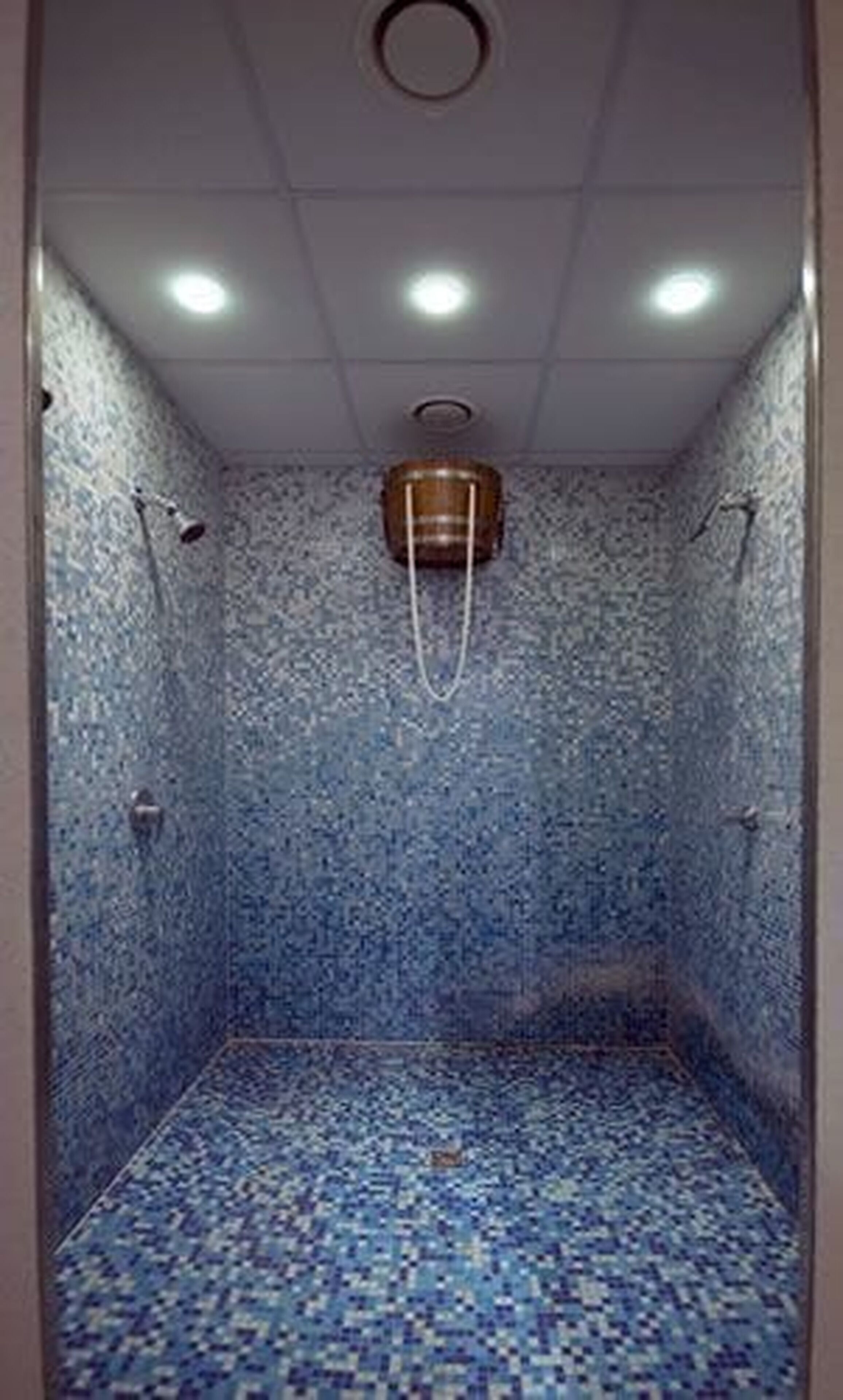 A small, tiled shower room with a single showerhead and a ceiling light.