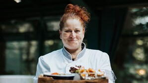 Una persona con uniforme de chef sostiene una bandeja con alimentos.