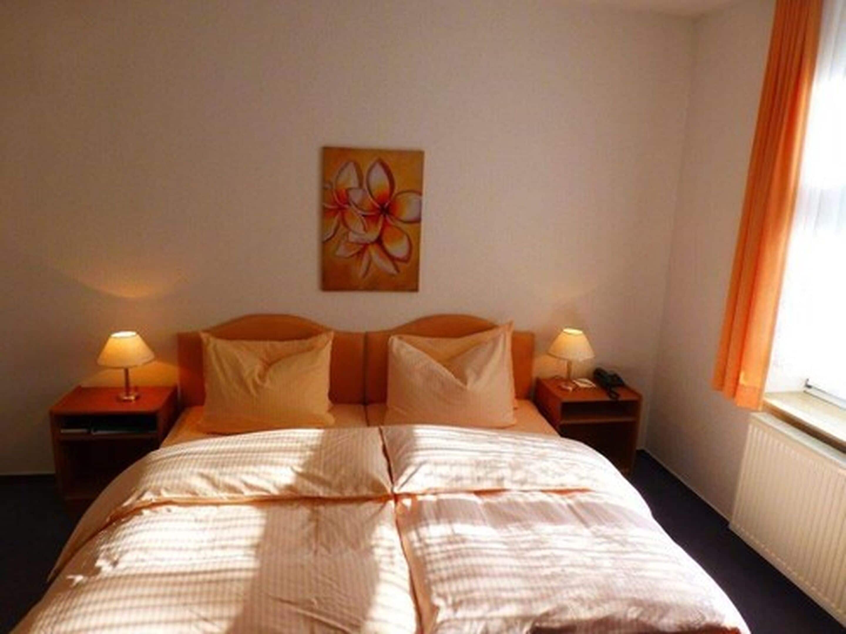 A hotel room with a bed, two bedside tables with lamps, a wall-mounted painting, and a window with curtains.