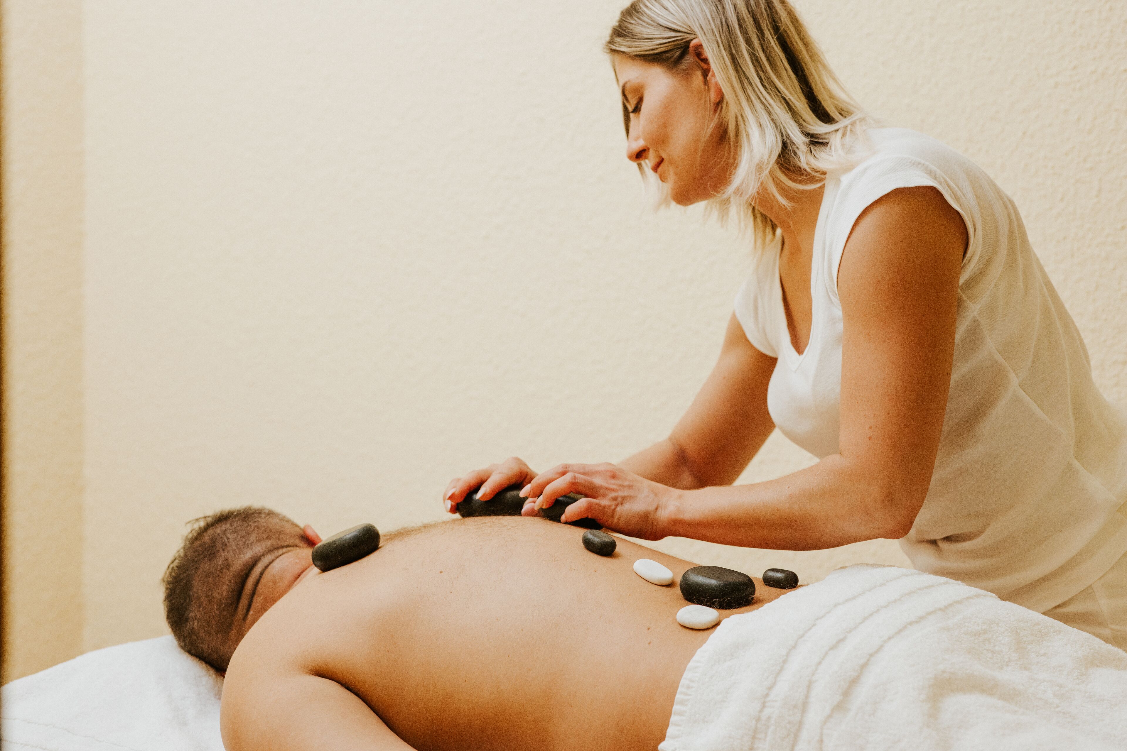 En person modtager en varm stenmassage på et hvidt håndklæde.